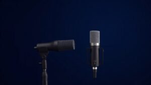 Two professional condenser microphones side by side on deep navy studio background, one large diaphragm model with wide capsule next to compact small diaphragm model, soft side lighting creates gentle shadows, clean modern product photography, photorealistic studio setup