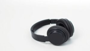Premium over-ear headphones folded flat on clean white studio background with soft side lighting. Modern black or dark grey finish. Clean minimal composition showing travel-ready design. Photorealistic product photography in 16:9 horizontal format.