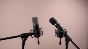 Two professional broadcast microphones on adjustable boom arms positioned at optimal interview angles against clean studio background with soft directional lighting emphasizing the microphone capsules and professional setup arrangement
