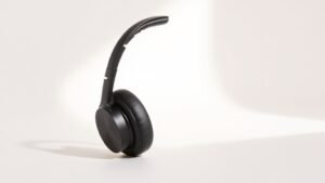 Modern wireless over-ear headphones in matte black positioned at slight angle on clean off-white studio background with soft side lighting creating subtle shadows