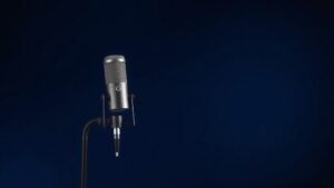 Professional condenser microphone on boom stand against clean deep navy studio background with soft side lighting highlighting the microphone capsule and body details in photorealistic modern minimal style