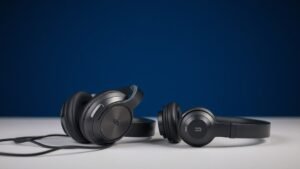 Premium wired headphones next to wireless bluetooth headphones on clean studio desk with deep navy background. Soft side lighting reveals cable detail and wireless design differences. Modern minimal product photography style.
