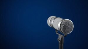 Professional studio condenser microphone positioned upright on shock mount against clean deep navy background with soft side lighting revealing metallic capsule details and acoustic mesh grille in sharp photorealistic detail horizontal format
