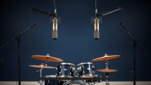 A matched pair of large diaphragm condenser microphones mounted on boom stands in an overhead position above a drum kit, photographed in a clean studio space with a deep navy background, soft side lighting revealing the metallic capsule detail, photorealistic, 16 by 9 horizontal format, no people, no text.