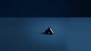 A single pair of sleek wireless noise-cancelling earbuds resting on a smooth matte surface against a deep navy background. The earbuds are compact and modern with a glossy finish, soft side lighting casting gentle highlights along their curved forms and charging case nearby. The composition is minimal and polished, emphasizing clean lines and premium materiality in a calm studio atmosphere.