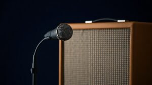 A large-diaphragm dynamic microphone on a low boom stand positioned close to the grille cloth of a vintage-style guitar amplifier cabinet, photographed against a deep navy studio background with soft directional side lighting, photorealistic product photography, 16:9 horizontal frame, no people, no text.