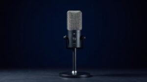 A single professional XLR microphone stands upright on a sleek desktop stand against a deep navy studio background. Soft directional side lighting catches the metallic mesh grille and polished body, casting a gentle shadow to one side. The microphone has a classic large-diaphragm capsule design with a matte black finish and subtle silver accents, giving the scene a clean, premium, editorial quality.