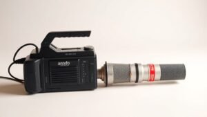 A professional portable field recorder and a large diaphragm condenser microphone placed side by side on a clean off-white studio surface, soft directional side lighting revealing texture and detail, no accessories, no cables, no hands, minimal composition, photorealistic, 16 by 9 horizontal format.