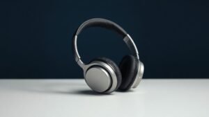 A single pair of premium over-ear headphones resting on a minimal white surface against a deep navy background. Soft diffused side lighting casts gentle shadows that highlight the sleek contours of the ear cups and polished headband. The mood is clean, refined and editorial, with a shallow depth of field adding subtle depth to the composition.