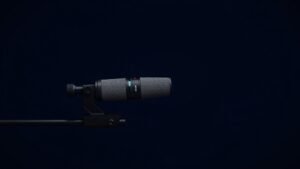 A professional shotgun microphone mounted on a studio boom pole lying horizontally against a deep navy background. Soft side lighting reveals the interference tube and body detail in photorealistic clarity. No people, no hands, no text, no accessories in frame. Clean minimal product photography at 16 by 9 aspect ratio.